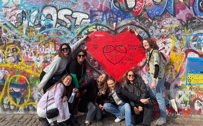 A group of students having their photo taken in front of a wall with graffiti