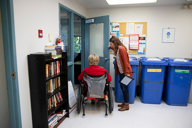 Jo Anthony, left, enters a room with the help of CapU student Alecia Ferreira at the North Shore Neighbourhood House in North Vancouver on Nov. 20, 2019. As part of the Unified Grant research funding program, CapU students are providing augmentative communication support to North Shore stroke survivors. (Photo by Taehoon Kim)