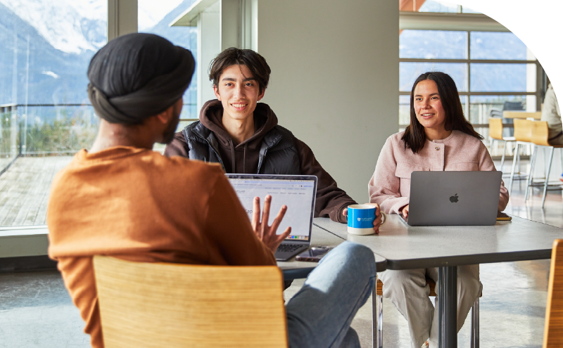 Three CapU students sitting in the Squamish Cafeteria having a conversation.