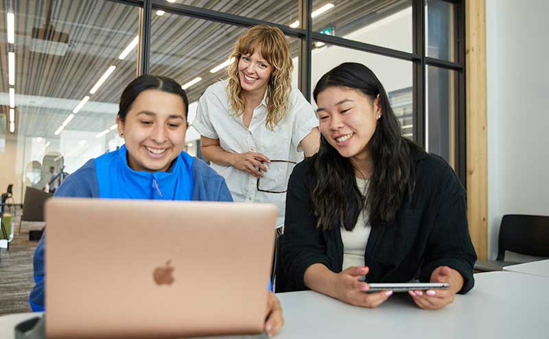 CapU students working on a computer with an admissions advisor in the background.