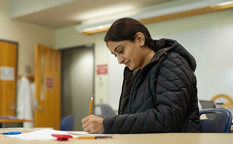 CapU student writing with a pencil at a desk.