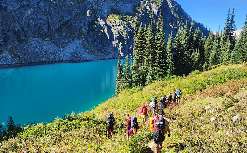 CapU Outdoor Recreation students on a hike with mountains and a lake in the background.