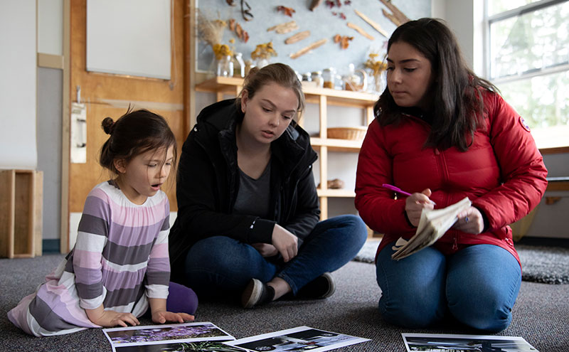Two ECCE students looking at pictures with a child.